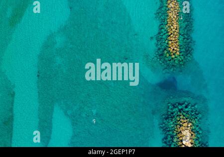 Aerial view of a barrier wall in the crystal clear blue ocean with ...