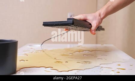 Man's hand turns over the keyboard and shakes out drops of spilled coffee Stock Photo