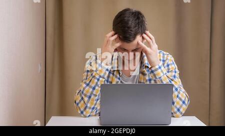 Young man angry typing on laptop at table Stock Photo