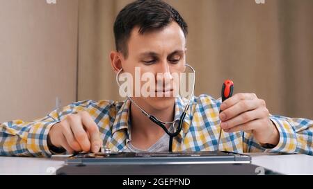 repairman removes the laptop cover and listens with a phonendoscope Stock Photo