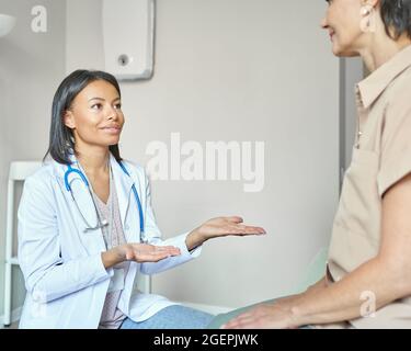 Young supportive afro american female doctor reaching hands out to help middle-aged woman patient Stock Photo