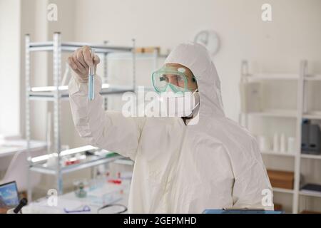 Biologist in protective laboratory clothing looks intently at a test tube with liquid in his hands. Stock Photo