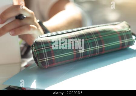 detail of a pen and pencil case from school with selective focus of a girl sitting next to the container on a sunny day Stock Photo