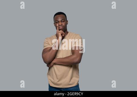 Dark-skinned young man in beige tshirt looking determined Stock Photo