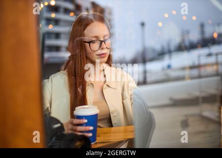 Concentrated young woman watching tutorial online on modern laptop device using wireless internet connection in cafe.Pensive professional female photo Stock Photo