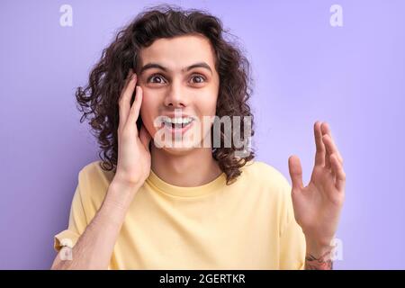 Surprised caucasian guy in casual yellow t-shirt isolated on purple background studio portrait. People lifestyle concept. Mock up copy space. Keeping Stock Photo