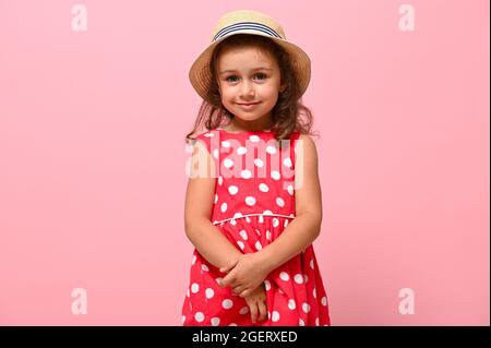 Little cute child kid baby girl 3-4 years old wearing pink polka dots dress, isolated on pink wall background, children studio portrait. Mother's Day, Stock Photo