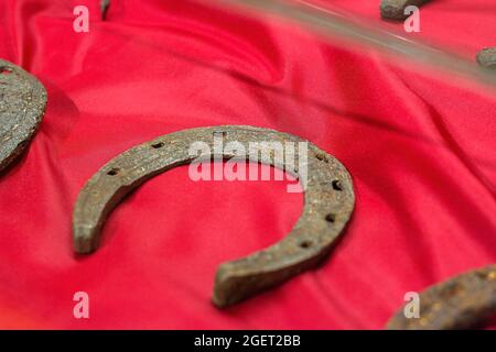 Old medieval rusty metal horseshoe in the museum on red background. Stock Photo
