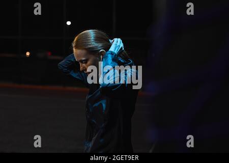 Focused serious redhead woman in sportive clothes at night city during jogging, having rest, looking down, taking a break. side view portrait. sport, Stock Photo