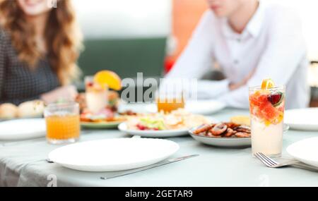 Cropped shot of young people friends gathered to dine together, sitting in restaurant at table with clean empty plates, snacks and drinks, family coup Stock Photo