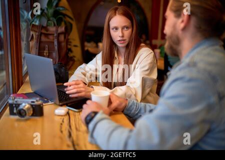 Serious Photographer Freelancer Woman Having Talk With Man, In Cafe During Work Using Laptop, Listen To Talk And Explain, Side View Portrait. Copy Spa Stock Photo