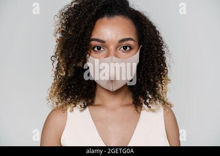 A close-up shot of the face of a curly-haired woman in a protective mask standing in the light studio Stock Photo