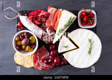 Charcuterie platter of assorted meats, cheeses and appetizers. Above view on a dark slate background. Stock Photo