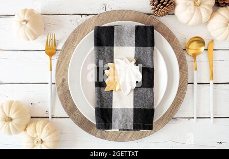 Autumn harvest or thanksgiving dinner table setting with plates, flatware, buffalo plaid napkin, pumpkins and decor. Top view on a white wood backgrou Stock Photo
