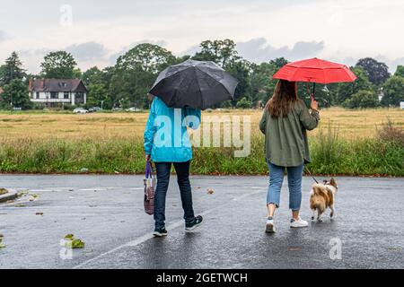WIMBLEDON LONDON, UK. 21 August 2021.  Two women with umbrellas walking with their dog during a rain shower in Wimbledon Common. The forecast is for rain and thunderstorms over the weekend in some parts of the UKCredit amer ghazzal/Alamy Live News