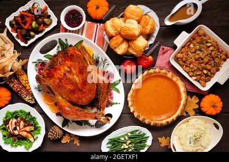 Classic Thanksgiving turkey dinner. Above view table scene on a dark wood background. Turkey, mashed potatoes, dressing, pumpkin pie and sides. Stock Photo