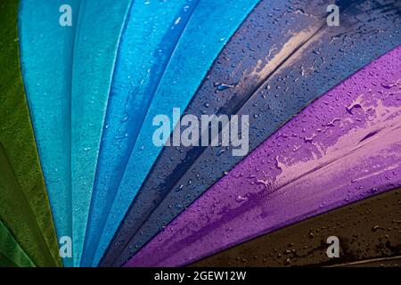 Wet waterproof textile surface of blue gradient colored umbrella under drizzle rain. Water drops dripping at blue purple umbrella fabric texture. Rain Stock Photo
