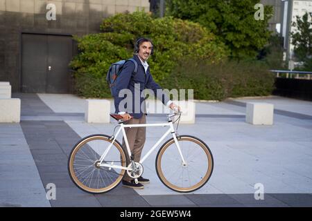 Bearded businessman, handsome and self-confident, carrying a backpack, walking outdoors with a bicycle. Eco-friendly transportation concept. High quality photo Stock Photo