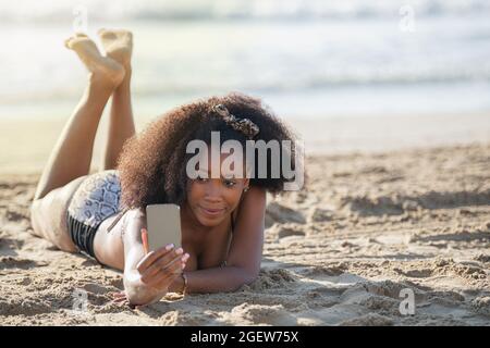 Young afro woman taking selfies with a mobile phone at the beach. Stock Photo