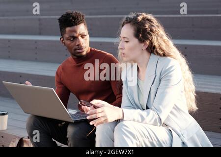 Two young confident colleagues discussing points of presentation at outdoor meeting Stock Photo