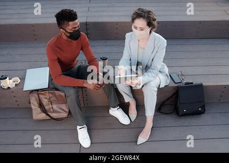 Two young multiracial colleagues in formalwear preparing presentation at outdoor meeting Stock Photo