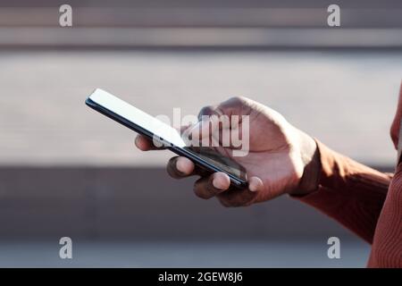 Hand of young African man with smartphone texting or scrolling through online stuff outdoors Stock Photo
