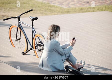 Back view of elegant businesswoman scrolling in smartphone while having rest outside Stock Photo