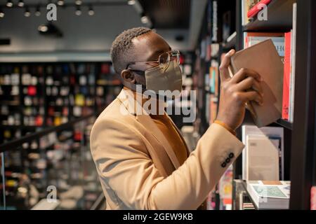 Young African man in smart casualwear choosing books in library or bookshop Stock Photo