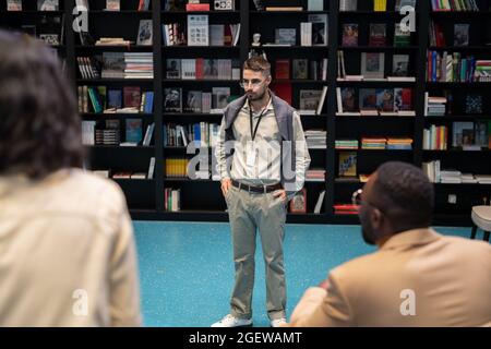 Strict young teacher or coach standing in front of intercultural students in library or bookstore Stock Photo