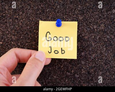 A woman holding an adhesive note with the words good job on it pinned on a cork bulletin board. Close up. Stock Photo