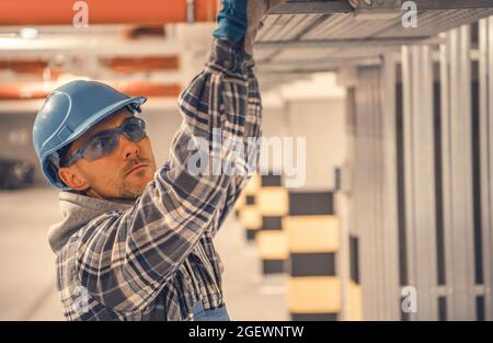 Caucasian Construction Engineer Wearing Blue Hard Hat and Eyes Protection Glasses Checking on Structure Elements. Industrial Theme. Stock Photo