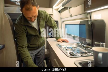 Road Trip and Van Life Theme. Caucasian Men in His 40s Preparing Camper Van RV Kitchen For Cooking. Stock Photo