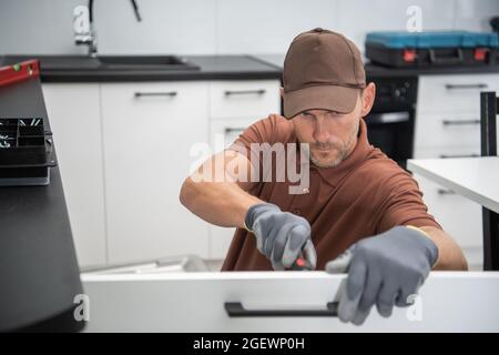 Caucasian Pro Cabinetmaker in His 40s Installing New Kitchen Furnitures. Worker Attaching Cabinet Wing Using Screwdriver. Home Remodeling. Stock Photo