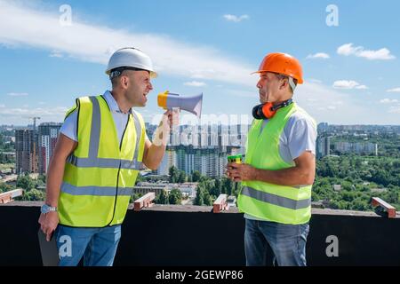 Angry boss yelling in megaphone at his builder on construction site Stock Photo