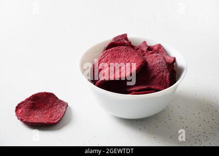 Vegetable beetroot chips in white bowl on a white background. Vegan snack. Close up. Stock Photo
