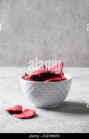 Vegetable beetroot chips in gray bowl on a gray background. Vegan snack. Close up. Vertical format. Stock Photo