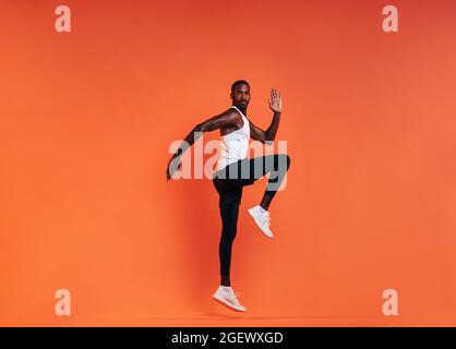 Young fit man doing exercises in studio. Male athlete jumping in the air over an orange background. Stock Photo