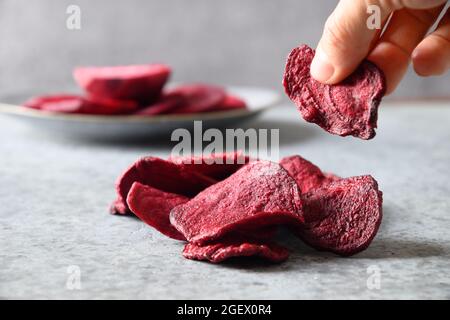 Take a piece vegetable beetroot chips on a gray background. Vegan snack. Close up. Stock Photo