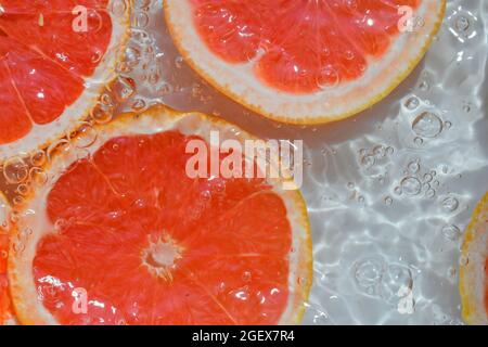 Slices of grapefruit in water on white background. Grapefruit close-up in liquid with bubbles. Slices of blood red ripe grapefruit in water. Macro Stock Photo
