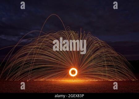 A wheel of fire created using steel wool alight on a bicycle wheel at night to provide a dark backdrop and orange sparks Stock Photo