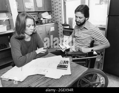 Austin Texas USA, circa 1992: Handicapped man in wheelchair and wife work on household budget from their kitchen table. ©Bob Daemmrich Stock Photo