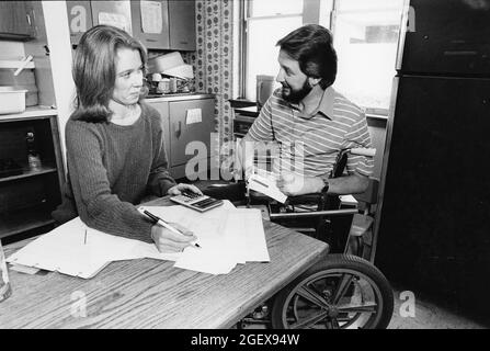 Austin Texas USA, circa 1992: Handicapped man in wheelchair and wife work on household budget from their kitchen table. ©Bob Daemmrich Stock Photo