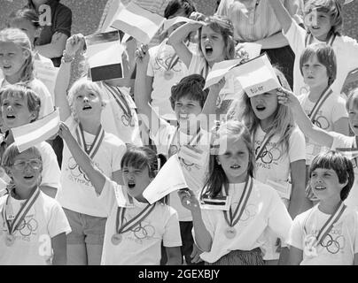 Austin Texas USA, circa 1992: Third grade students wearing t-shirts with Olympic rings and mock Olympic medals around their necks wave flags from different nations as they celebrate their school's Olympics-themed track-and-field day. ©Bob Daemmrich Stock Photo