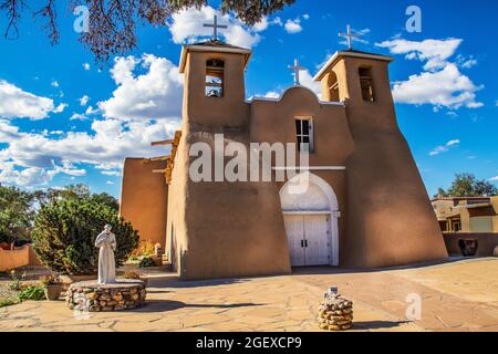 Historic adobe San Francisco de Asis Mission Church in Taos New Mexico in dramatic late afternoon light under intense blue sky with fluffy while cloud Stock Photo