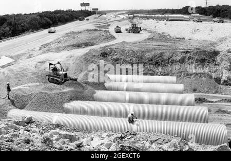 Austin Texas USA, circa 1984: Workers and heavy machinery lay pipes for drainage during construction of the Loop 360 highway in west Austin. ©Bob Daemmrich Stock Photo