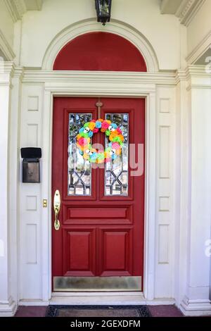 Resentails red front door with leaded glass in white house colorful Day of the Dead Halloween wreath Stock Photo