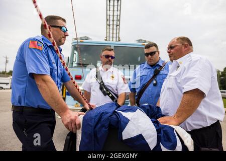 SPENCER, INDIANA - AUGEST 18: Firefighters wait to help raise an American flag for the funeral procession of fallen paramedic Brandon Staley on August 18, 2021 on W. Morgan Street in Spencer, Indiana. Staley died from a heart attack while working as a paramedic for Owen County EMS. Staley had just responded to a vehicle accident and was in an ambulance with crash survivors helping them on the way to a hospital when he himself became ill. Stock Photo