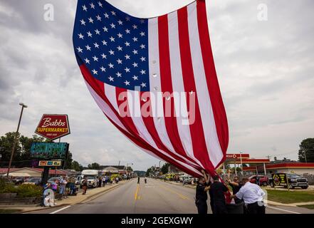 SPENCER, INDIANA - AUGEST 18: Firefighters raise an American flag for the funeral procession of fallen paramedic Brandon Staley on August 18, 2021 on W. Morgan Street in Spencer, Indiana. Staley died from a heart attack while working as a paramedic for Owen County EMS. Staley had just responded to a vehicle accident and was in an ambulance with crash survivors helping them on the way to a hospital when he himself became ill. Stock Photo