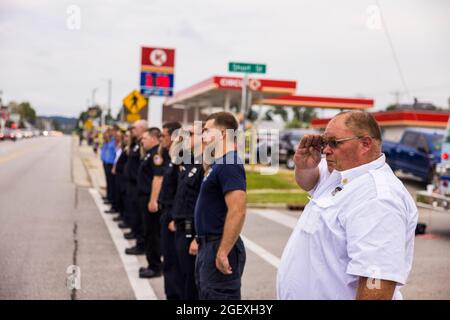 SPENCER, INDIANA - AUGEST 18: Firefighters render honors during the funeral procession of fallen paramedic Brandon Staley on August 18, 2021 on W. Morgan Street in Spencer, Indiana. Staley died from a heart attack while working as a paramedic for Owen County EMS. Staley had just responded to a vehicle accident and was in an ambulance with crash survivors helping them on the way to a hospital when he himself became ill. Stock Photo