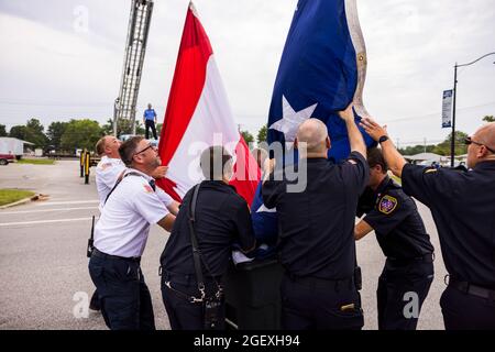 SPENCER, INDIANA - AUGEST 18: Firefighters lower an American flag after the funeral procession of fallen paramedic Brandon Staley on August 18, 2021 on W. Morgan Street in Spencer, Indiana. Staley died from a heart attack while working as a paramedic for Owen County EMS. Staley had just responded to a vehicle accident and was in an ambulance with crash survivors helping them on the way to a hospital when he himself became ill. Stock Photo